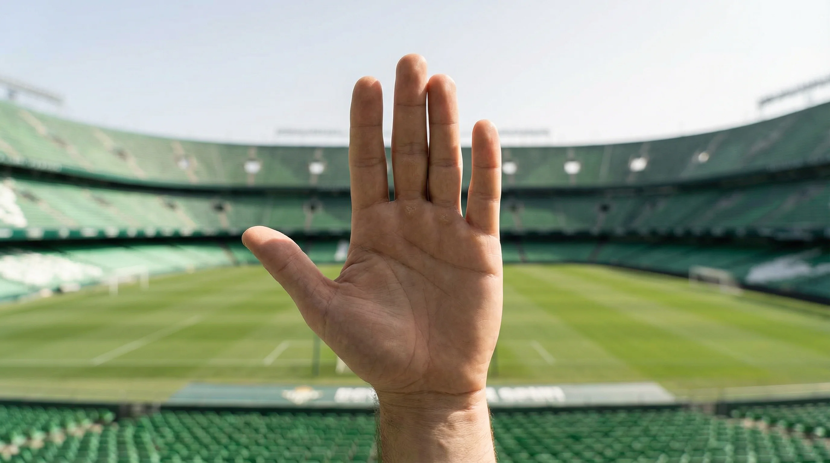 Apuestas responsables: mano mostrando señal de stop frente a un estadio de fútbol